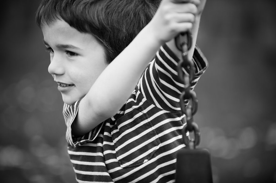 Boy looks to the left as he holds on to a chain 