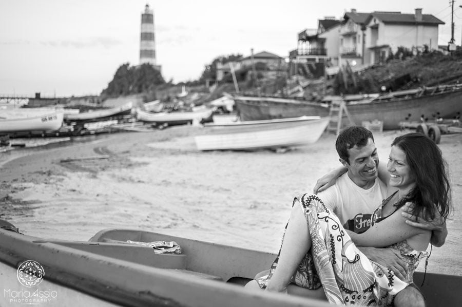 Couple sitting in a boat on the beach with a lighthouse, boats and fishing huts, destination wedding photographer Black Sea Evening pre wedding shoot