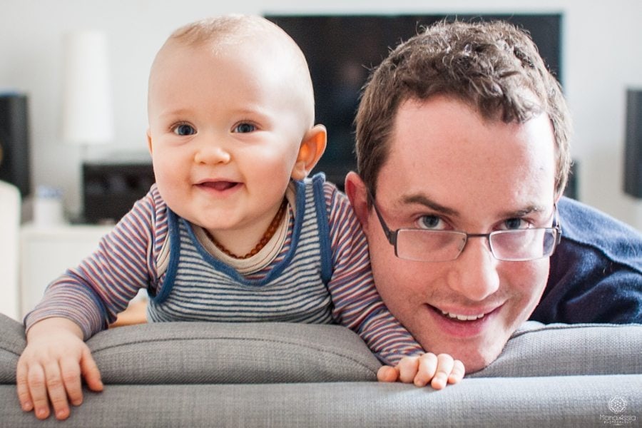 father and son smiling over the edge of a sofa