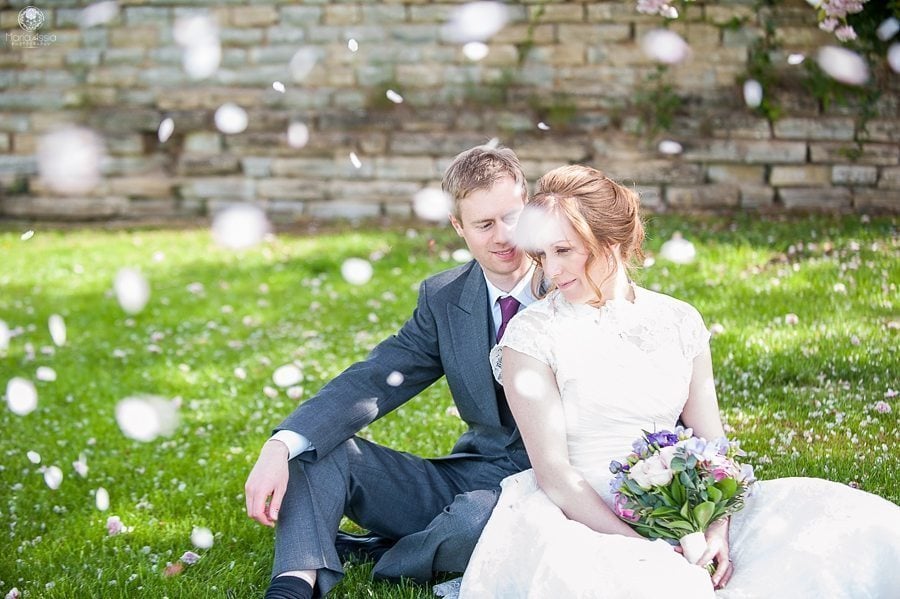 Bride and groom sitting with cherry blossoms falling around them at their Billesley Manor Hotel Fuchsia Spring Wedding 