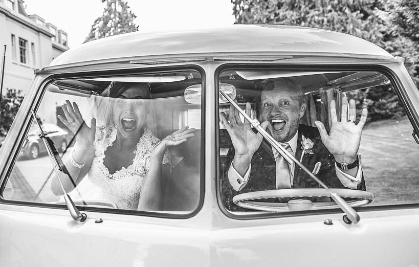 Bride and groom pulling faces in a white VW van in front of Coworth Park