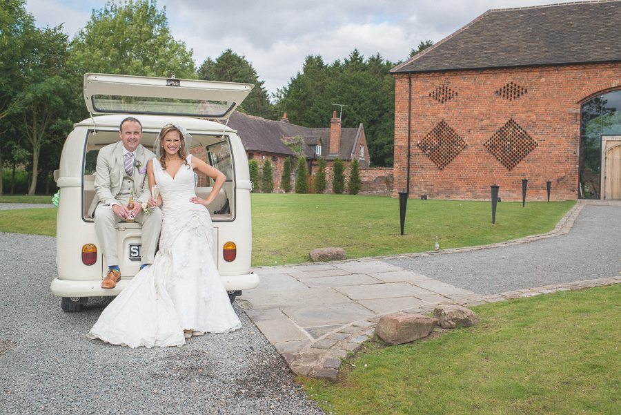 Bride and groom smiling at their VW wedding van in front of Shustoke Farm Barns