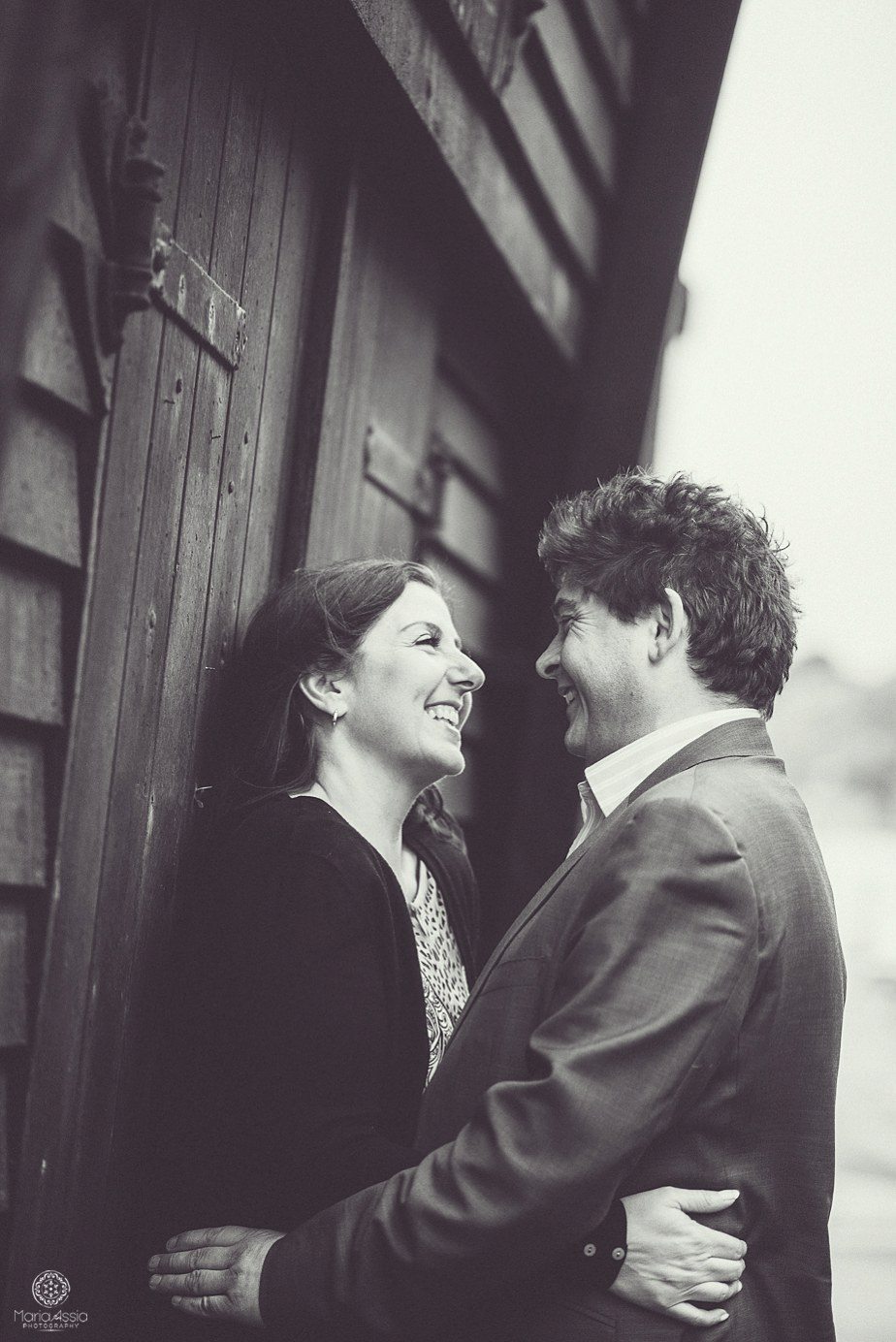 A couple laughing at each other leaning against a black Hastings fishing hut