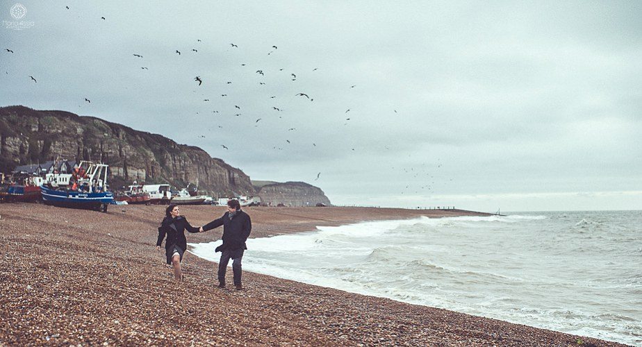 A couple walking along a windy beach at their Hastings pre wedding shoot