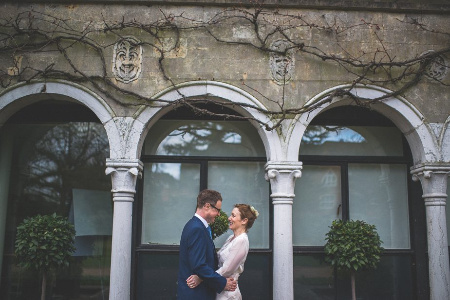 A bride and groom standing by the arches at Warren House