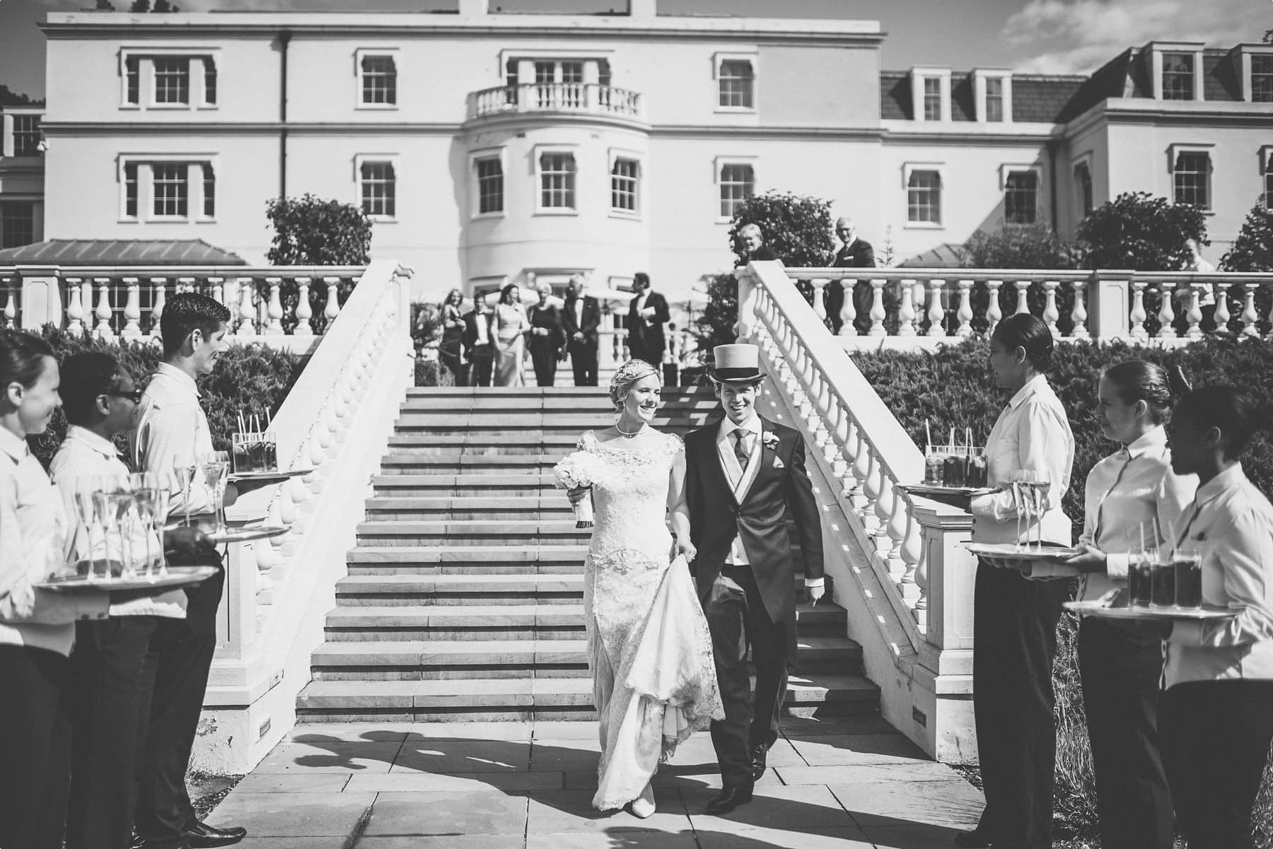 Bride and groom walking down Coworth Park mansion steps