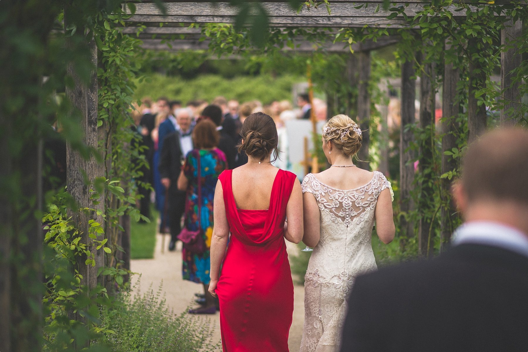 Bride and bridesmaid walking through the grounds at her Coworth Park Barn Summer wedding to join the other guests