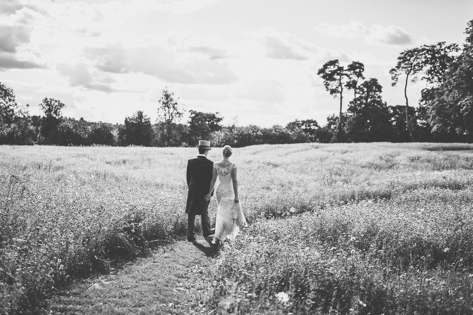 Bride and Groom walking into Coworth Park barn summer wedding wildflower meadow