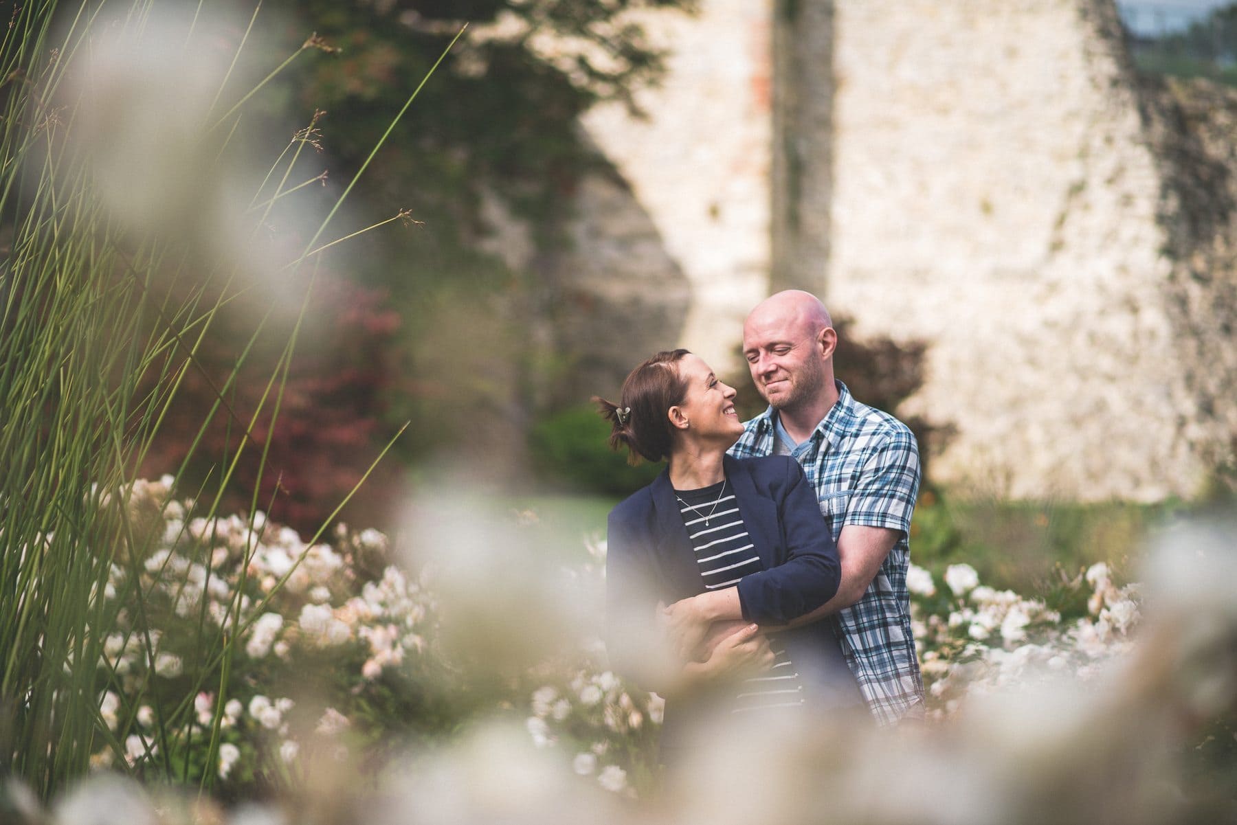 A girl looks up at her fiancé surrounded by summer flowers at their Farnham Castle engagement shoot