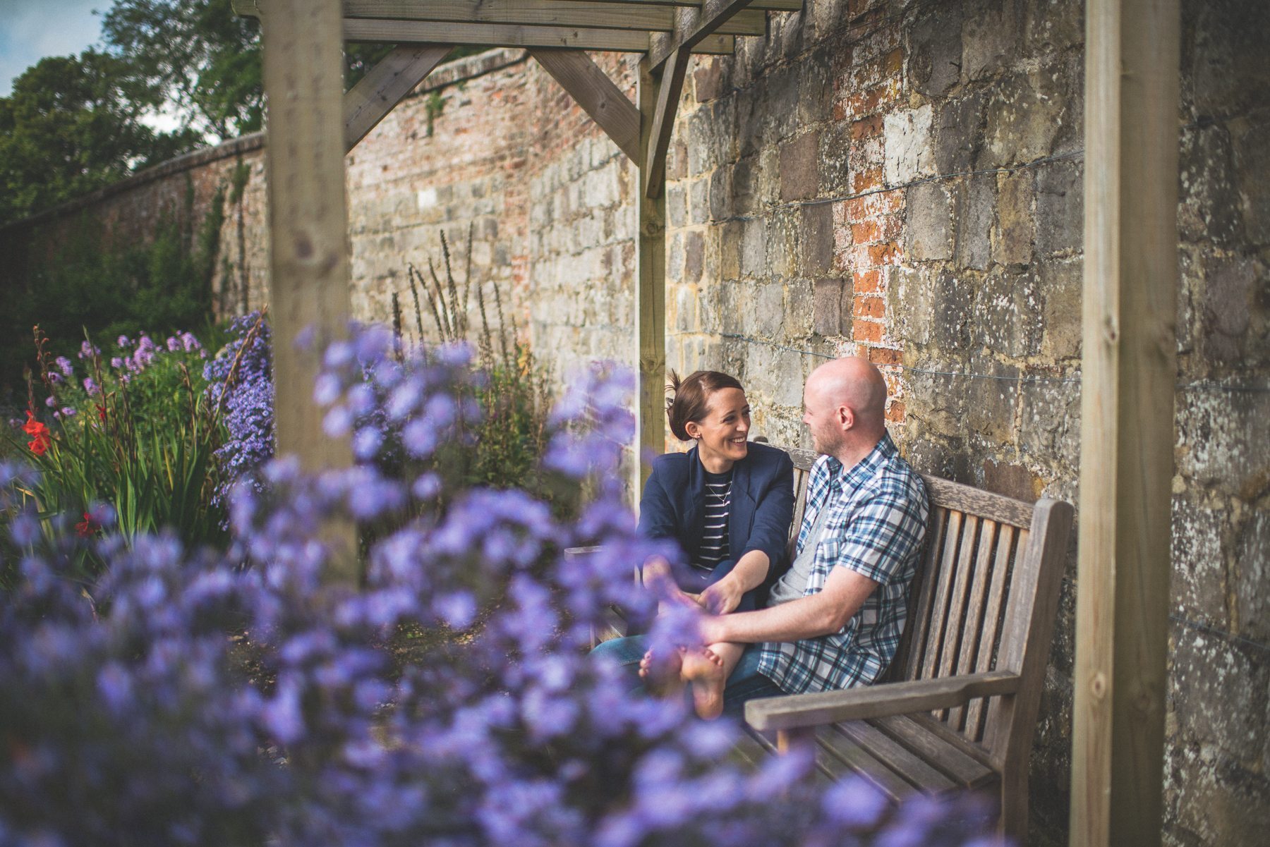 Farnham Castle Misty early morning engagement shoot couple laughing together as they sit on a bench