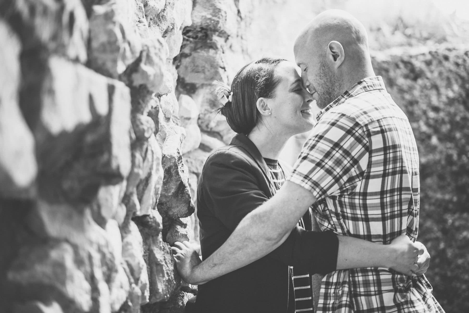 engaged couple kiss and hug against the stone wall at at Farnham Castle's Keep