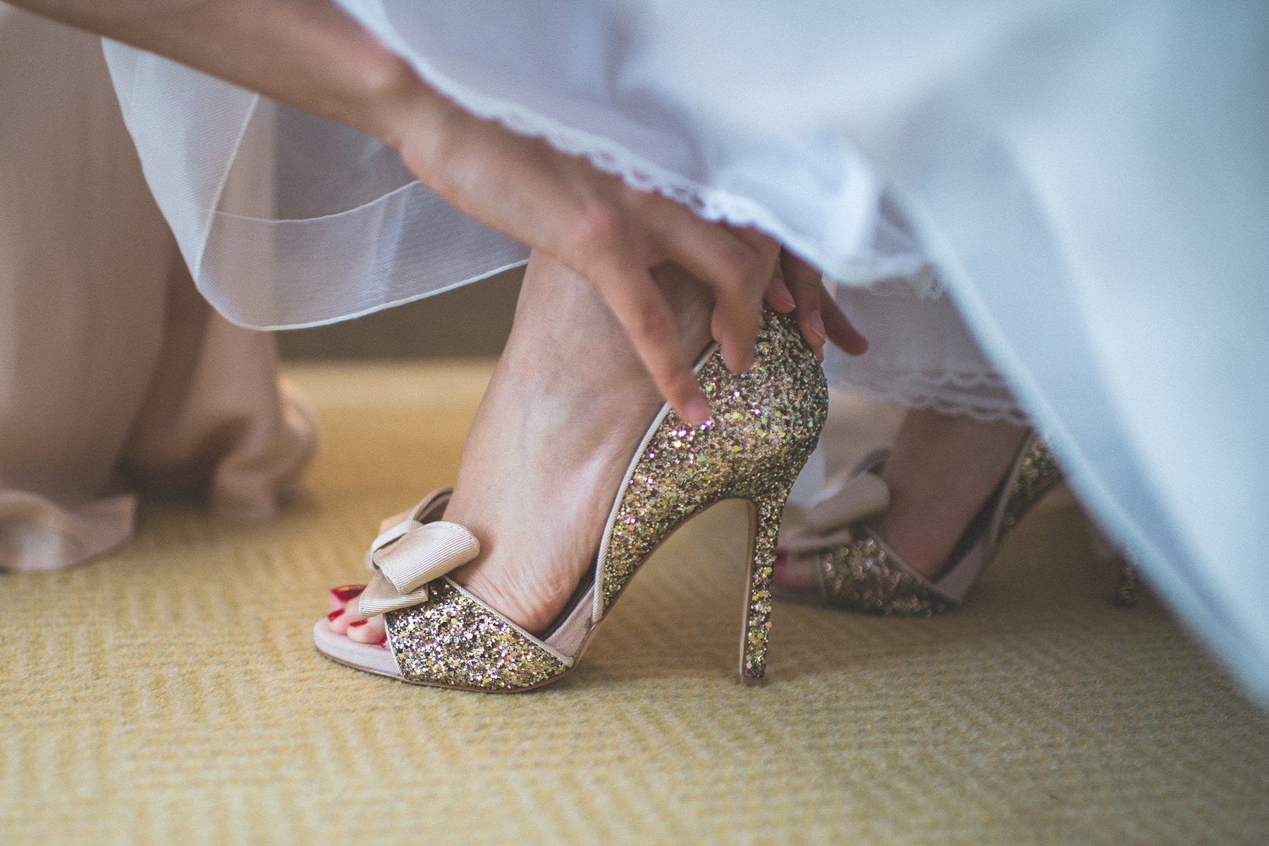 Bridesmaid putting on the bride's gold glitzy sparkly wedding shoes at the Chelsea Harbour Hotel wedding