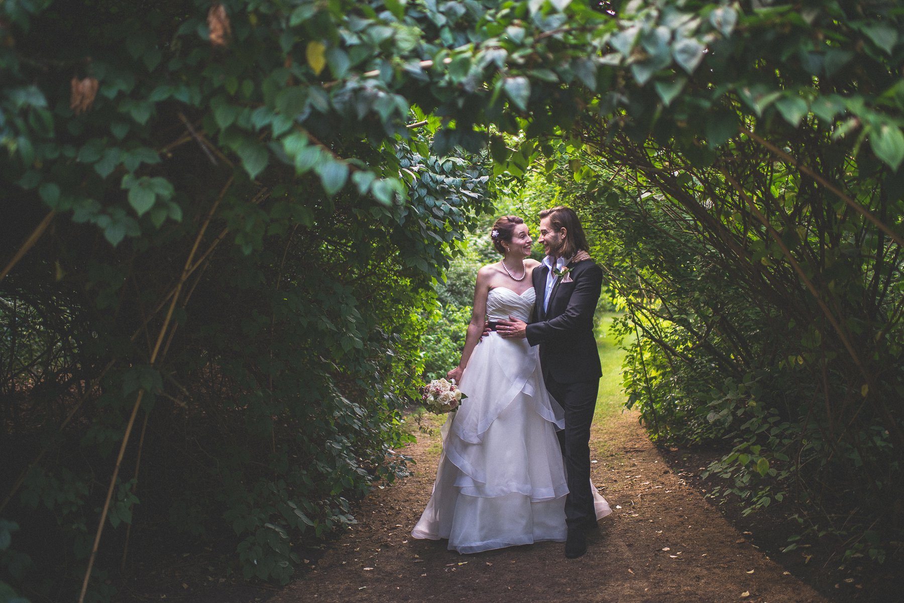 Bride and groom grinning at each other under a vine arch at Chelsea's Hurlingham Club