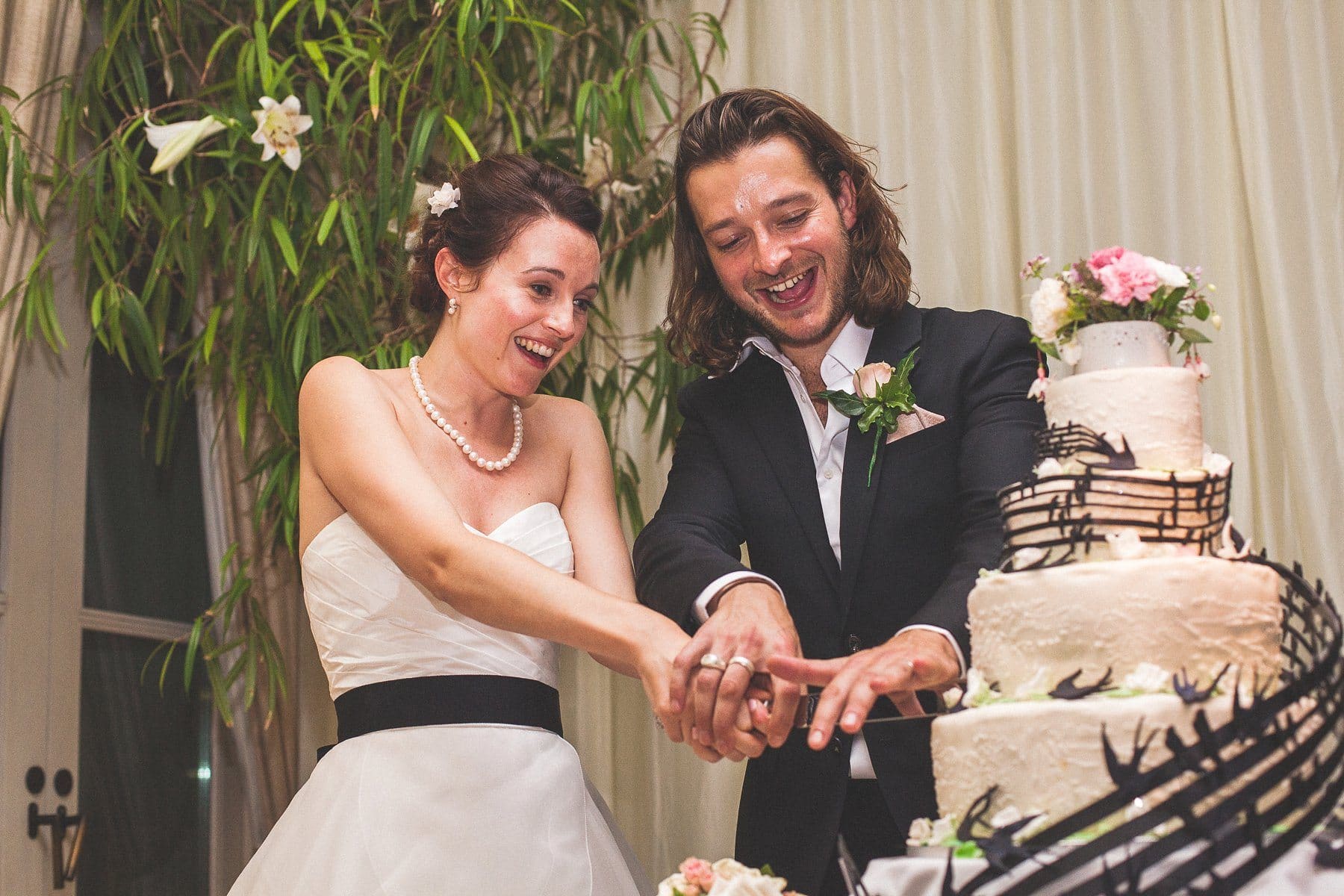 Hurlingham Club Bride and groom cutting their creative homemade music themed Chelsea wedding cake with swallows as musical notes