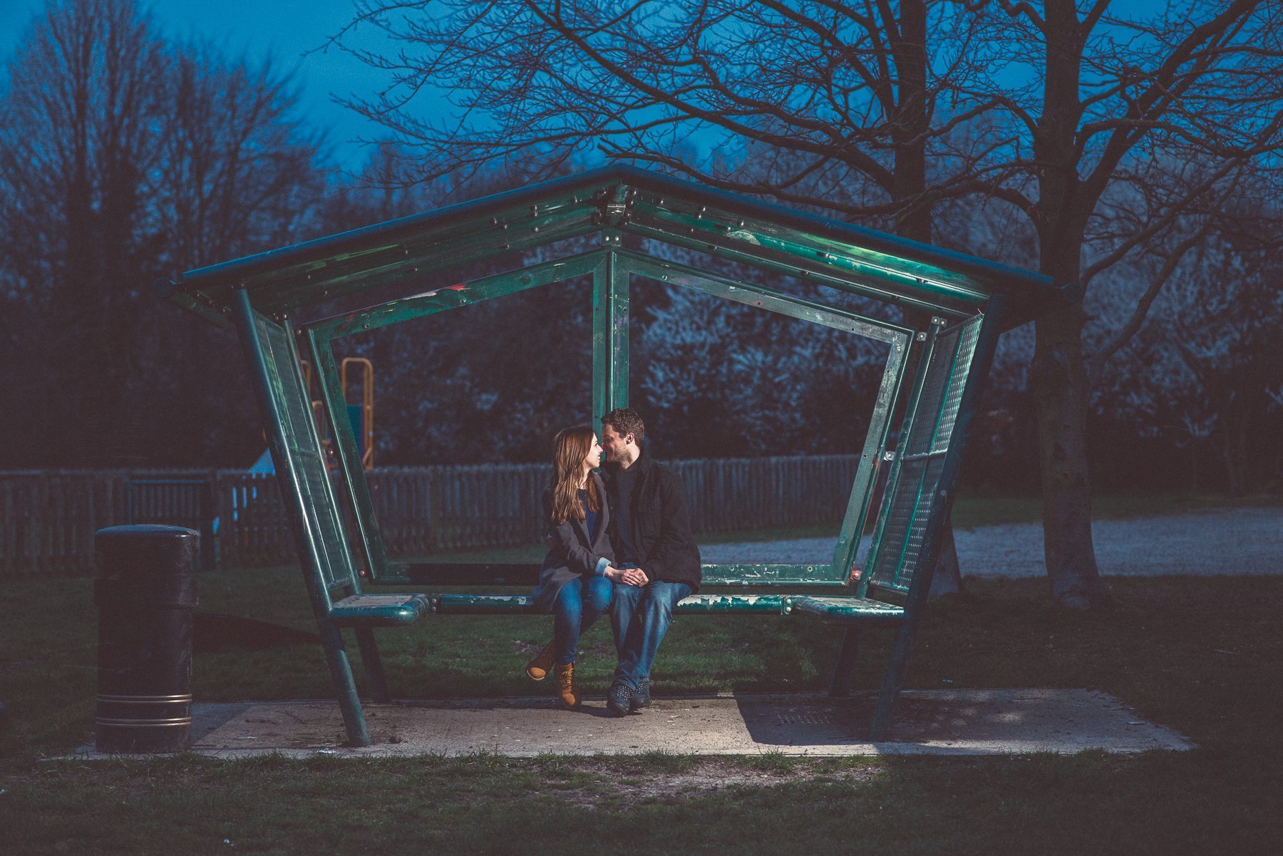 Romantic relaxed engagement shoot of a couple sitting on a bench in a park in the Kent Downs