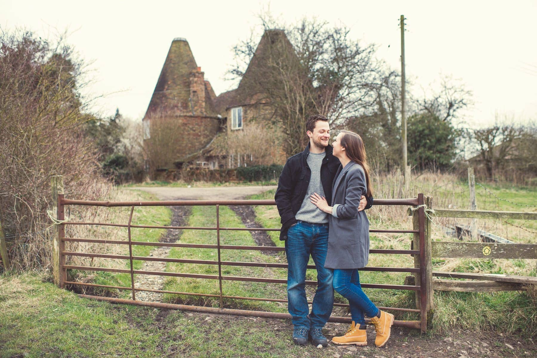 Kent Downs engagement shoot with a couple standing in front of two Oast Houses overlooking St Julians Club