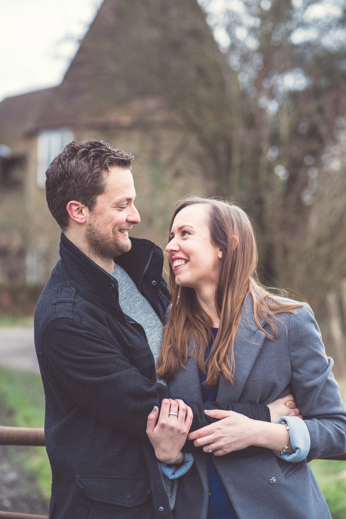 Engaged Couple looking at each other in front of an Oast House overlooking St Julians Club in Sevenoaks