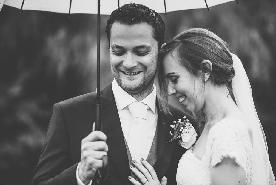 Bride and groom laughing in the rain under their umbrella at Smeetham Hall Barn