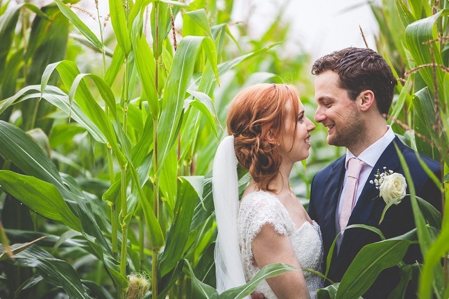 Bride and Groom smile at each other in a corn field at their rustic Smeetham Hall Barn wedding