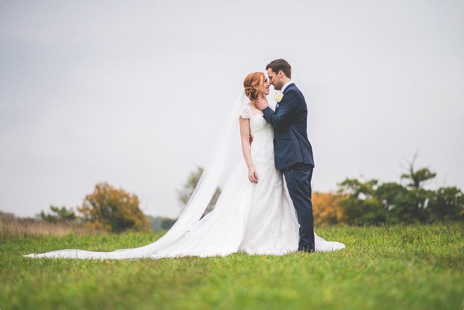 Bride and groom hugging in a field with a long wedding veil trailing behind them