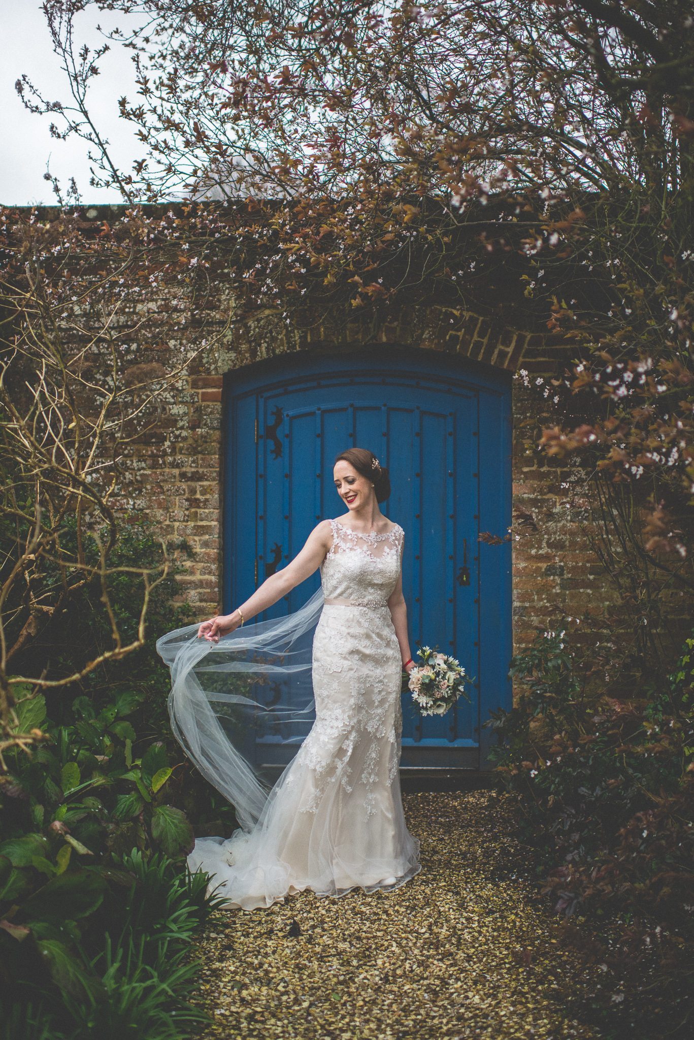 Bride holds her windswept veil in front of the Blue Gate at Farnham Castle Bishops Palace 