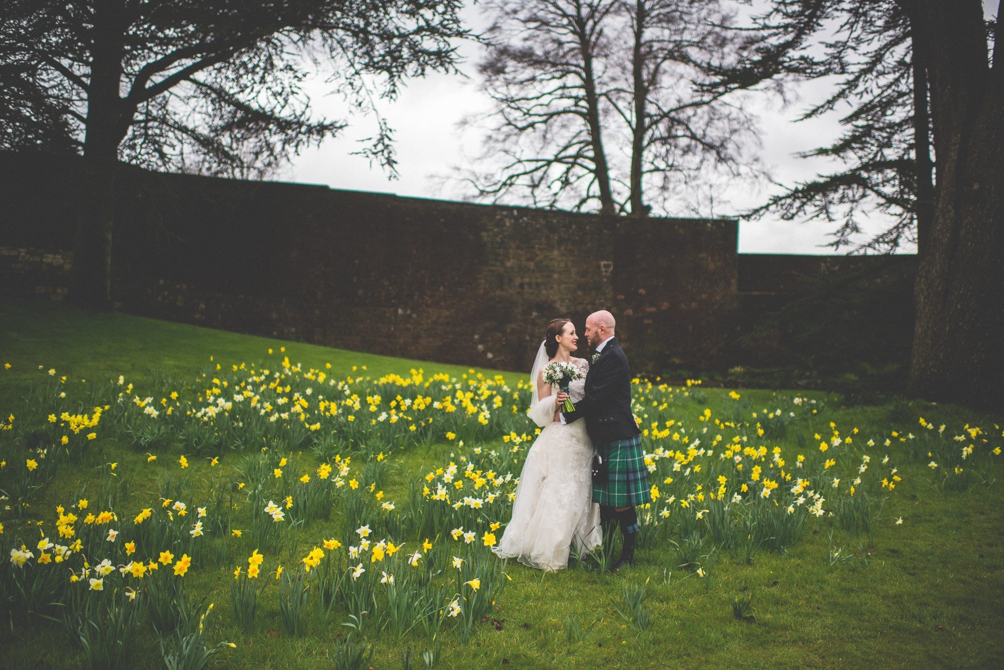 Scottish Bride and Groom stand surrounded by Daffodils in the grounds of Farnham Castle