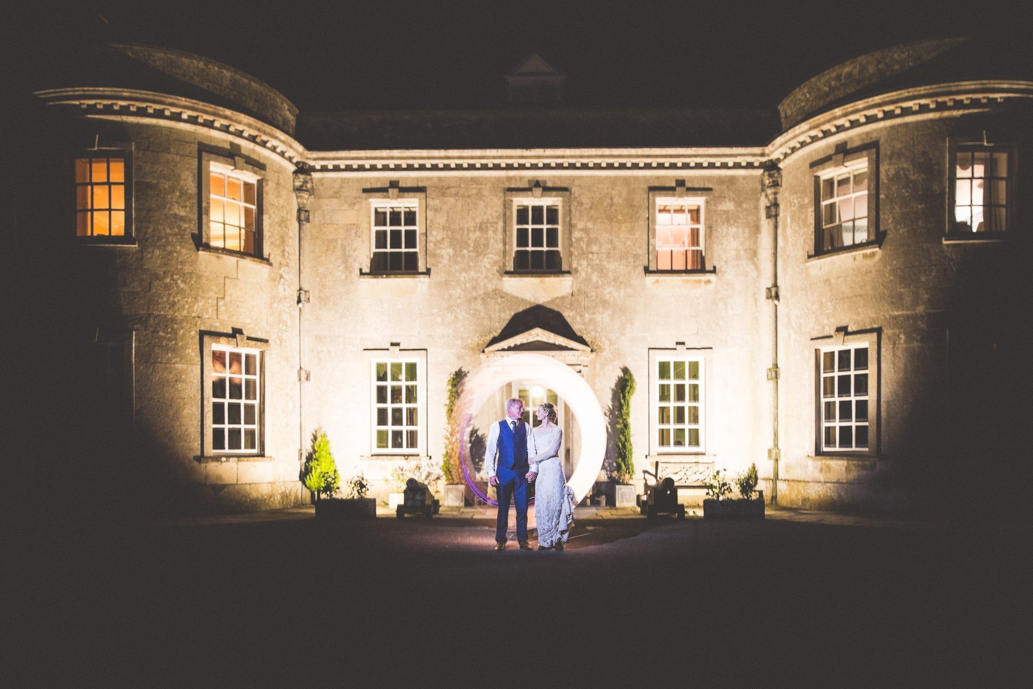 Bride and groom stand outside Smedmore House at night, lit by a light circle