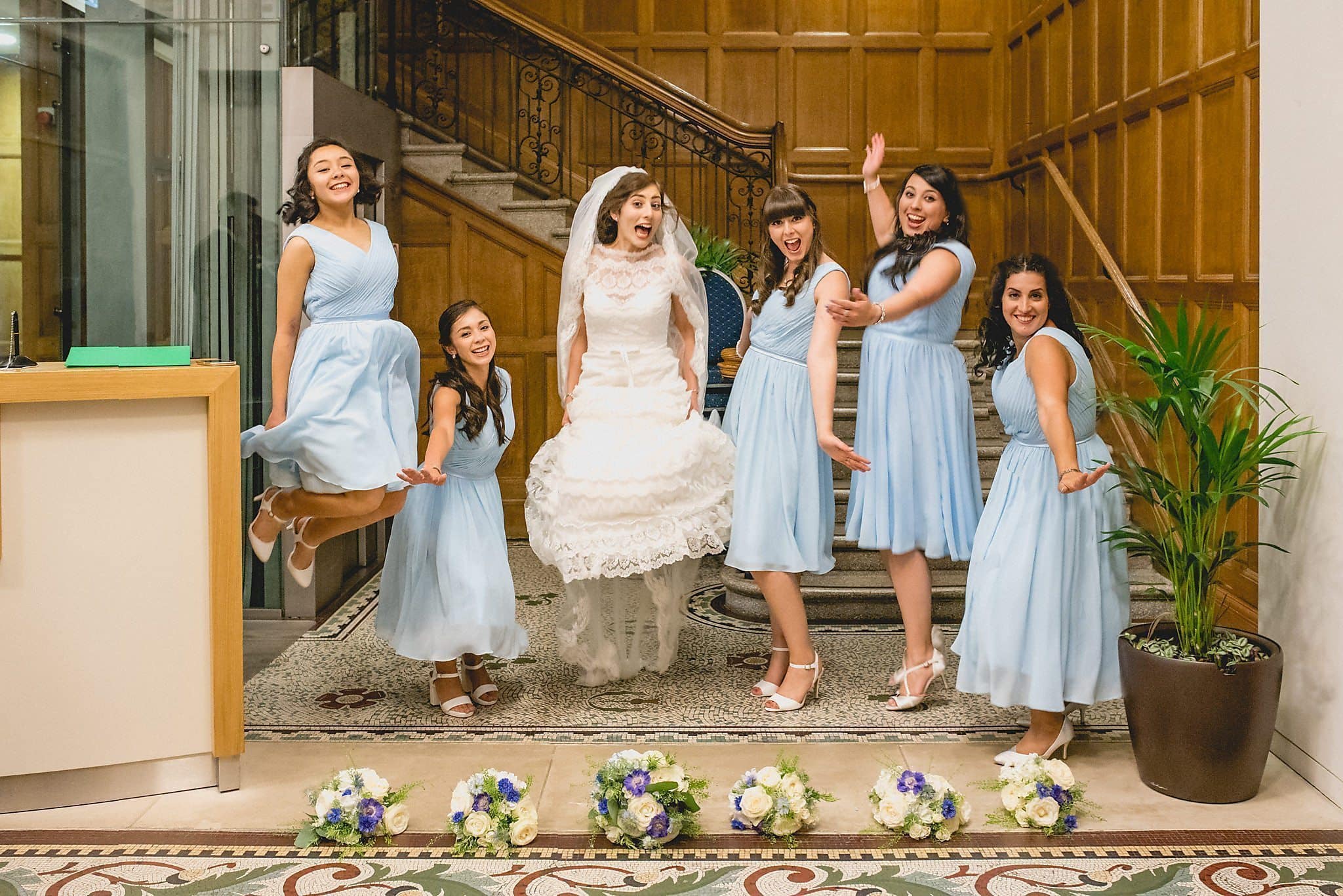 Bride jumping with her bridesmaids at the Royal Horticultural Halls staircase | Start Wedding Planning top tips