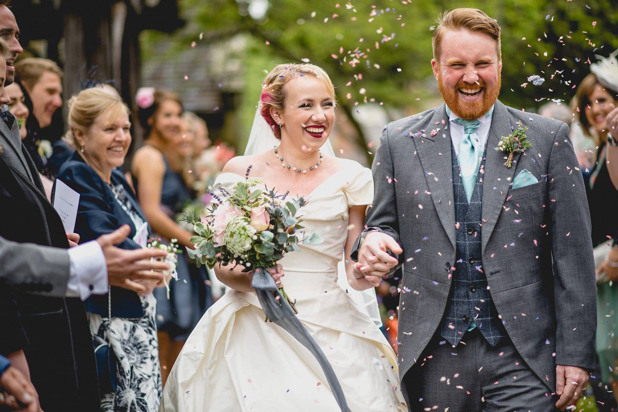 The newlyweds walk through the churchyard in a shower of petal confetti