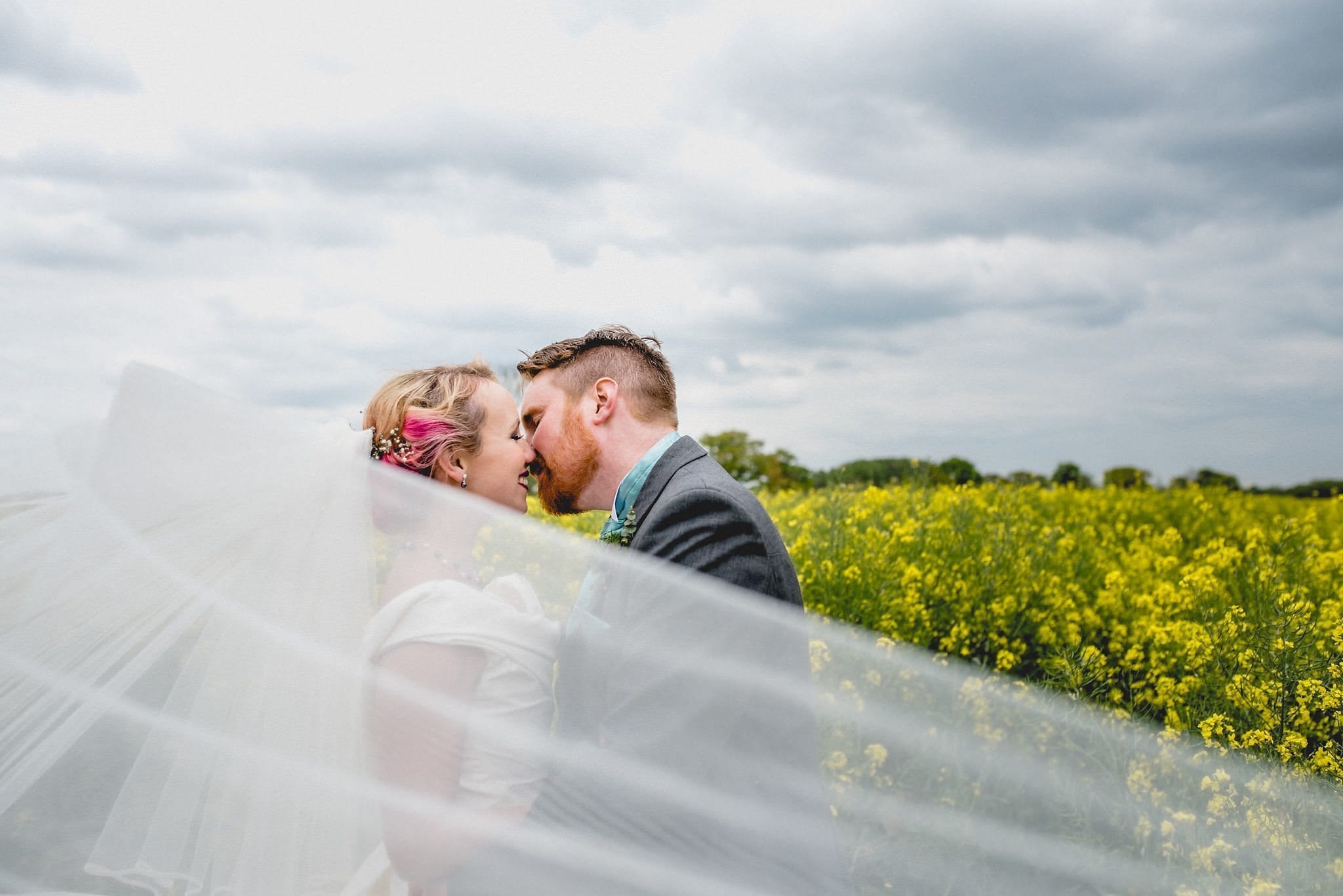 Bride and groom kiss in a field of bright yellow rapeseed flowers