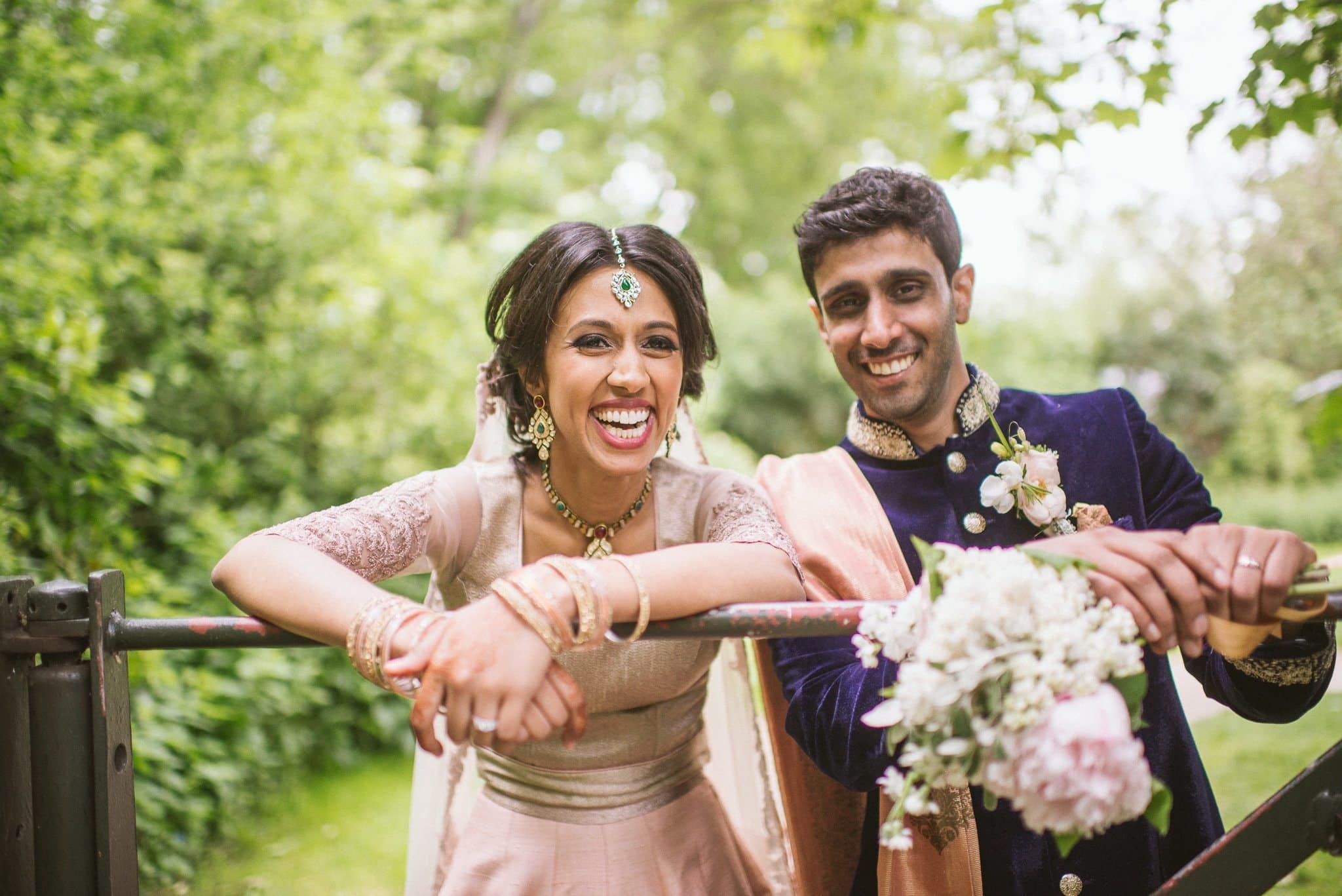 Bride and groom lean over a gate laughing | Start Wedding Planning