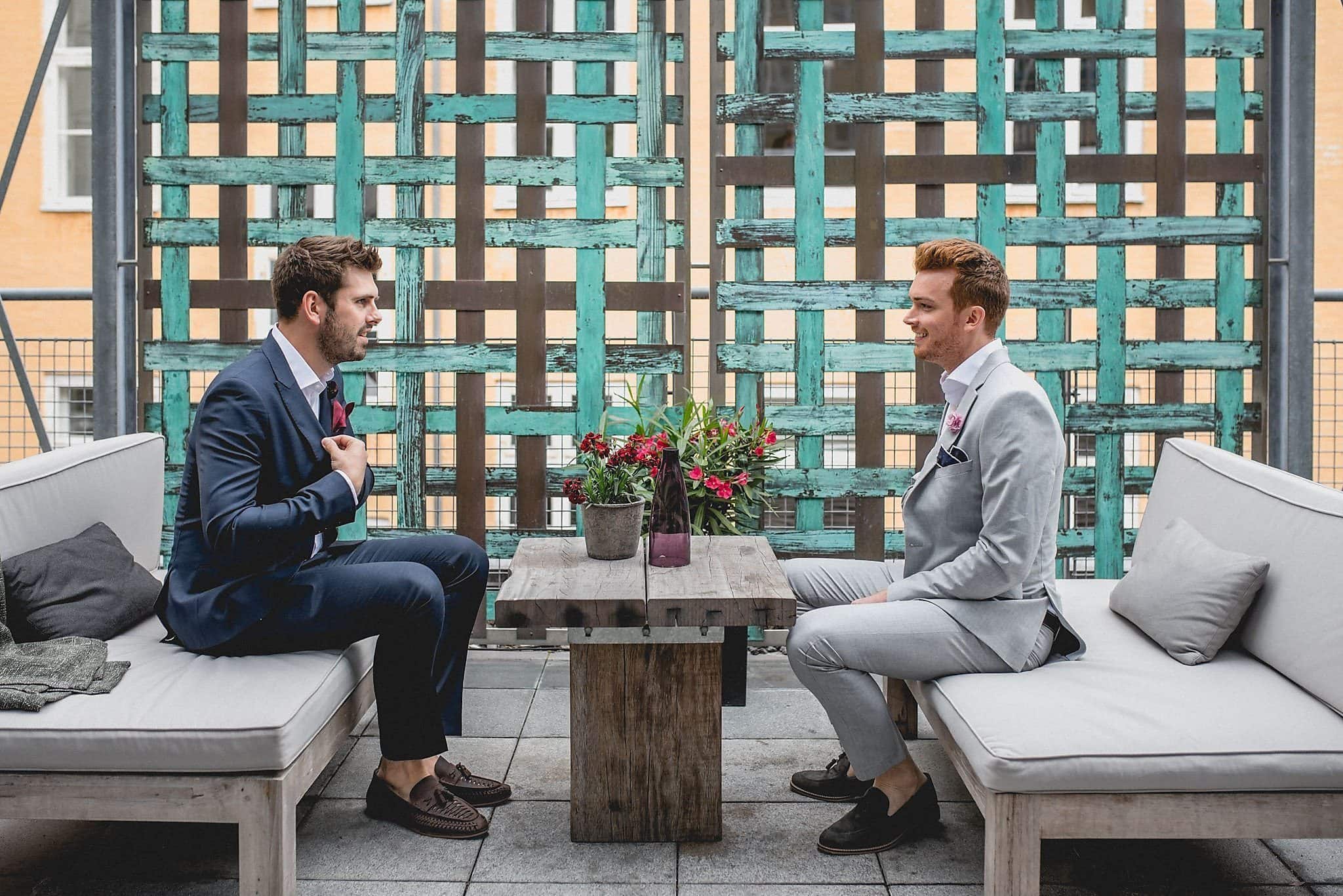 Two grooms sitting opposite each another on the roof terrace of their stylish Copenhagen hotel