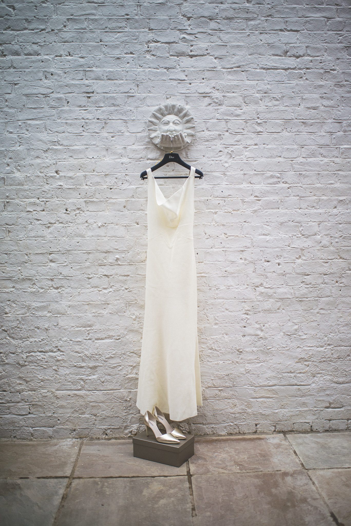 Ilaria's Dior gown and gold Armani shoes hang in front of a white brick wall