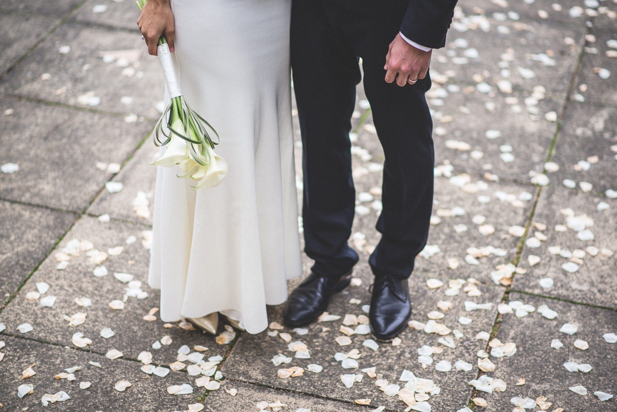 A three-quarter length shot of Marco and Ilaria from the waist down, standing amid the petal confetti after their wedding ceremony