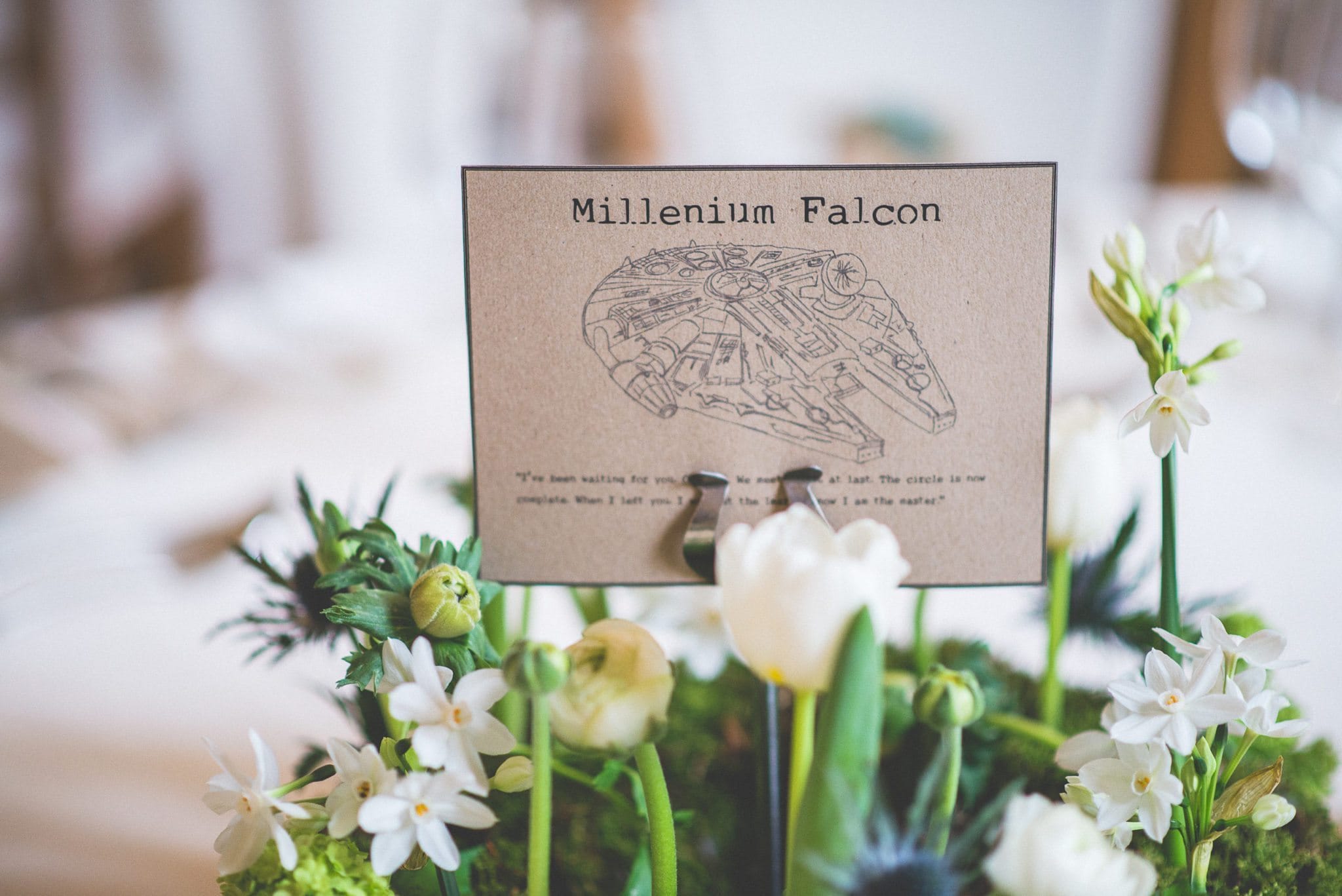 A close up of one of the table centres, showing the Millenium Falcon printed on rustic card among white flowers.