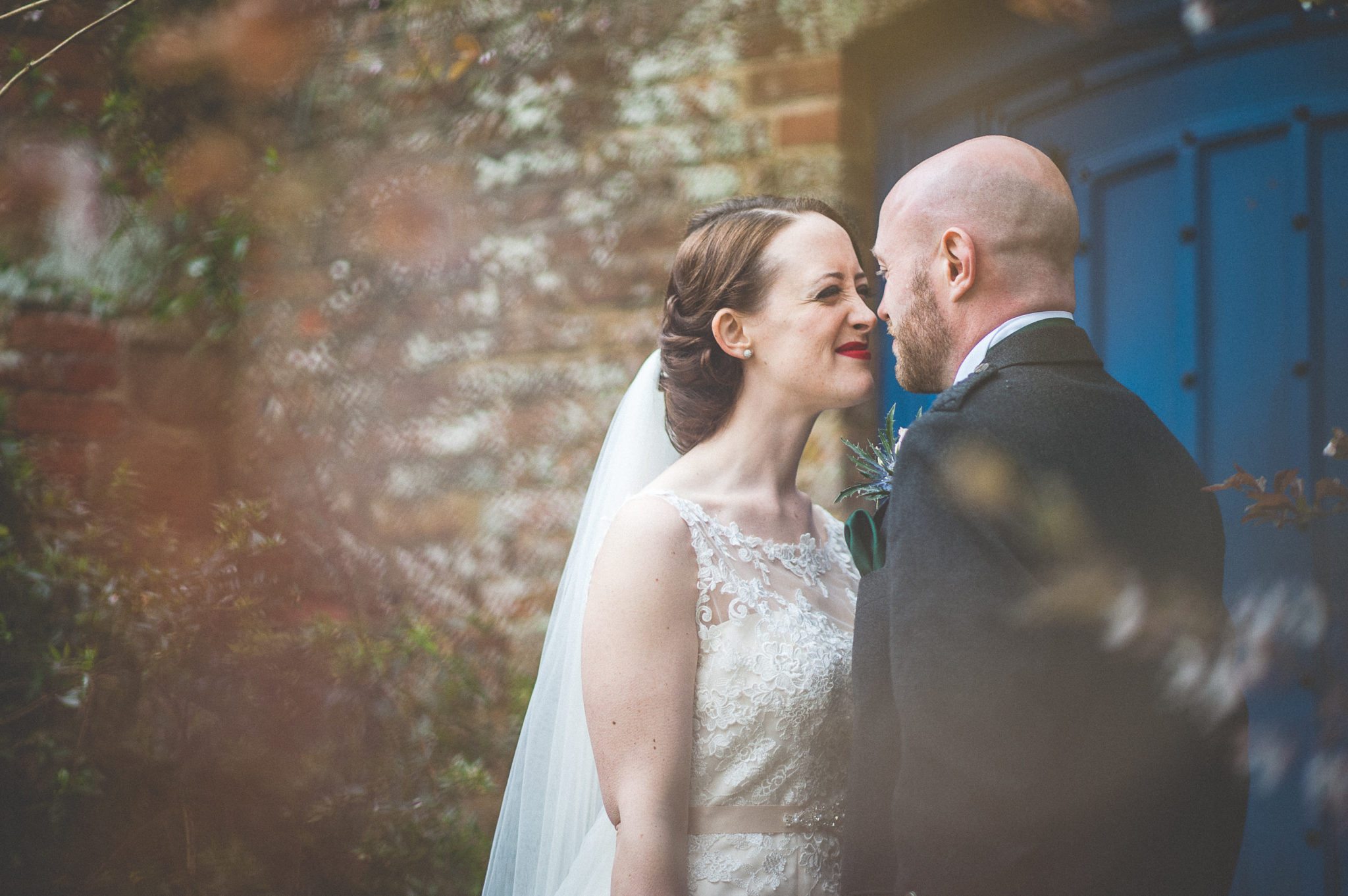 Bride and Groom smile at each other in front of a blue door at Farnham Castles Bishops Palace