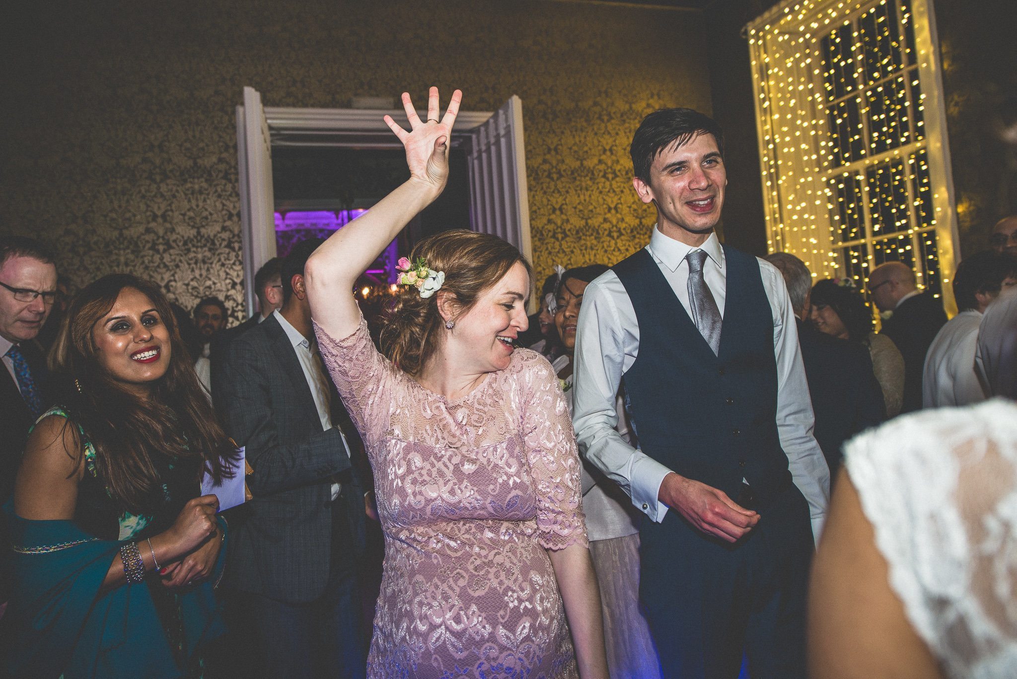 A heavily pregnant bridesmaid in a pink lace dress rocks out on the dancefloor