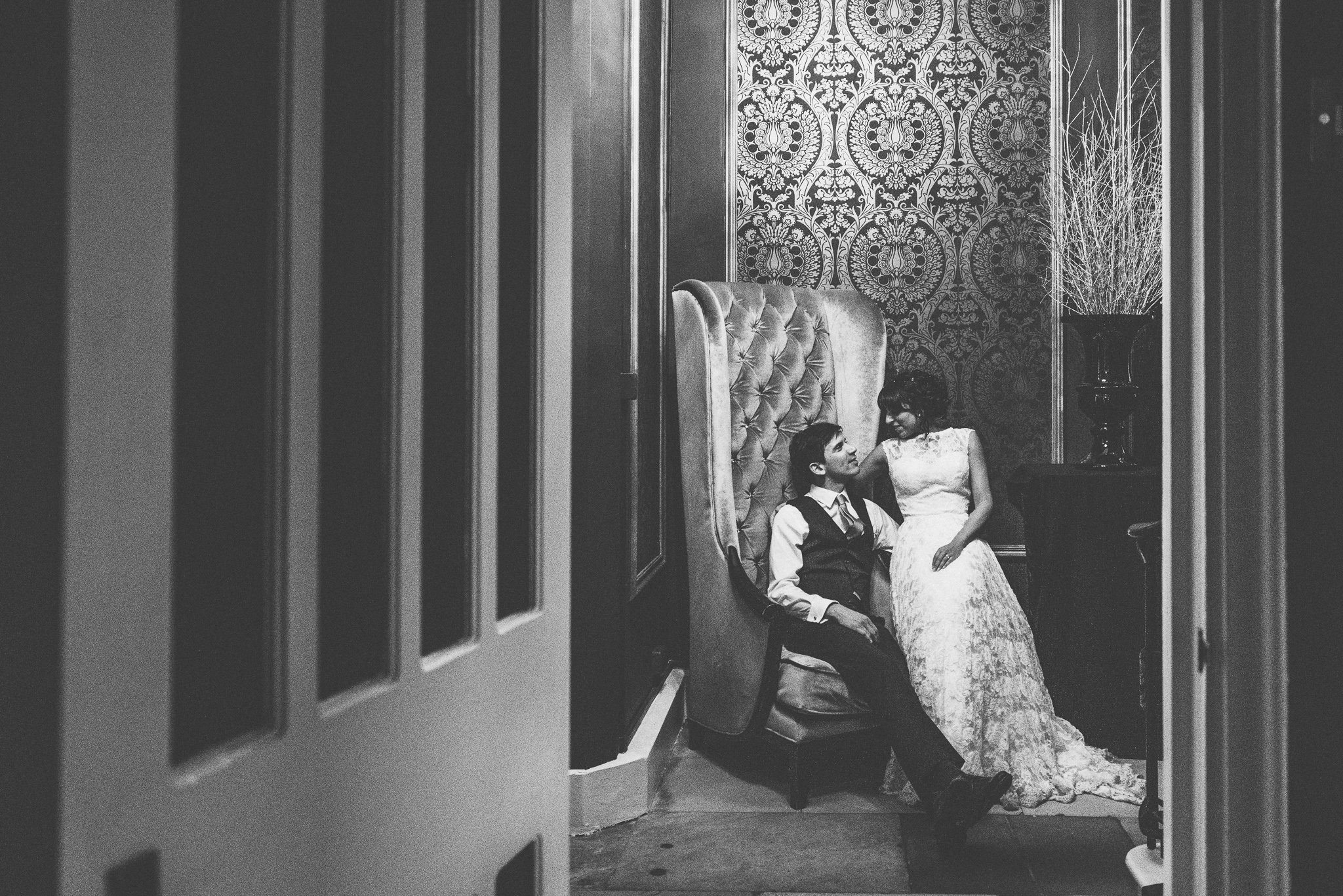 Bride and groom cuddle together in a tall chair at the end of the night at Nonsuch Mansion