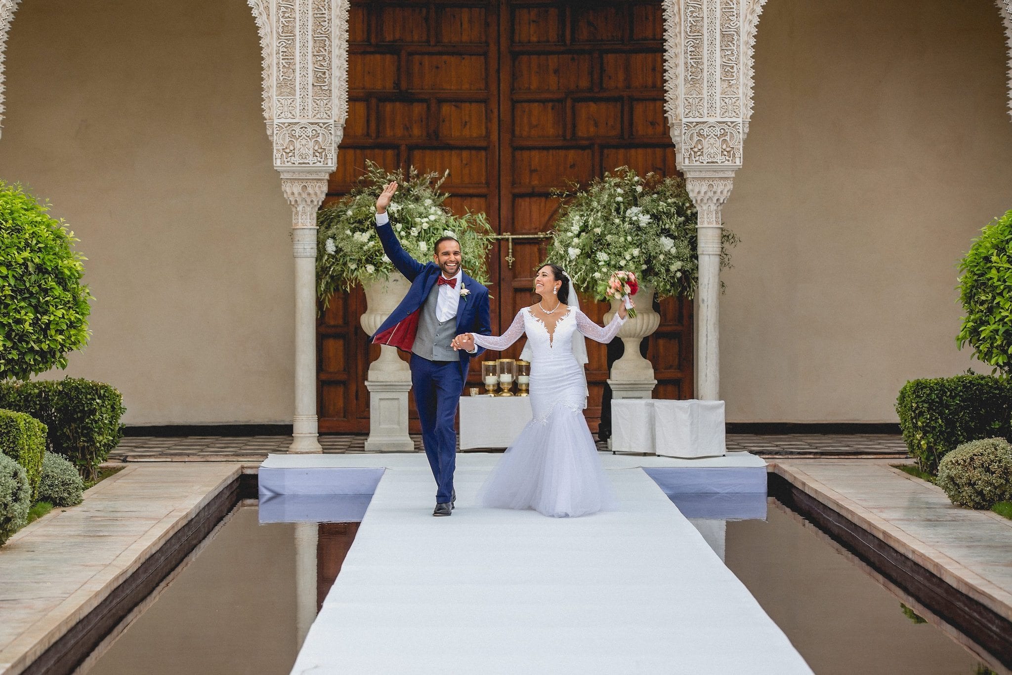 Bride and groom walk up the aisle at their Morocco destination wedding waving at their wedding guests