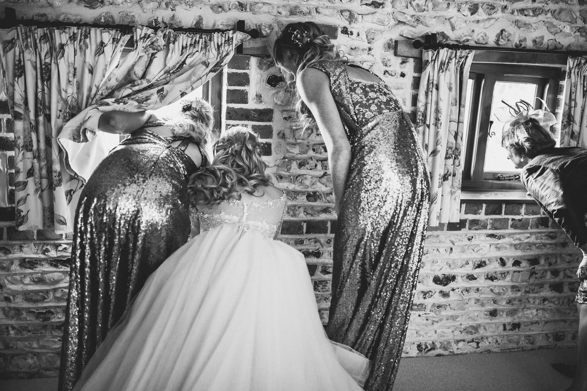 Bride and Bridesmaids looking out the window at the Upwaltham Barns wedding guests arriving