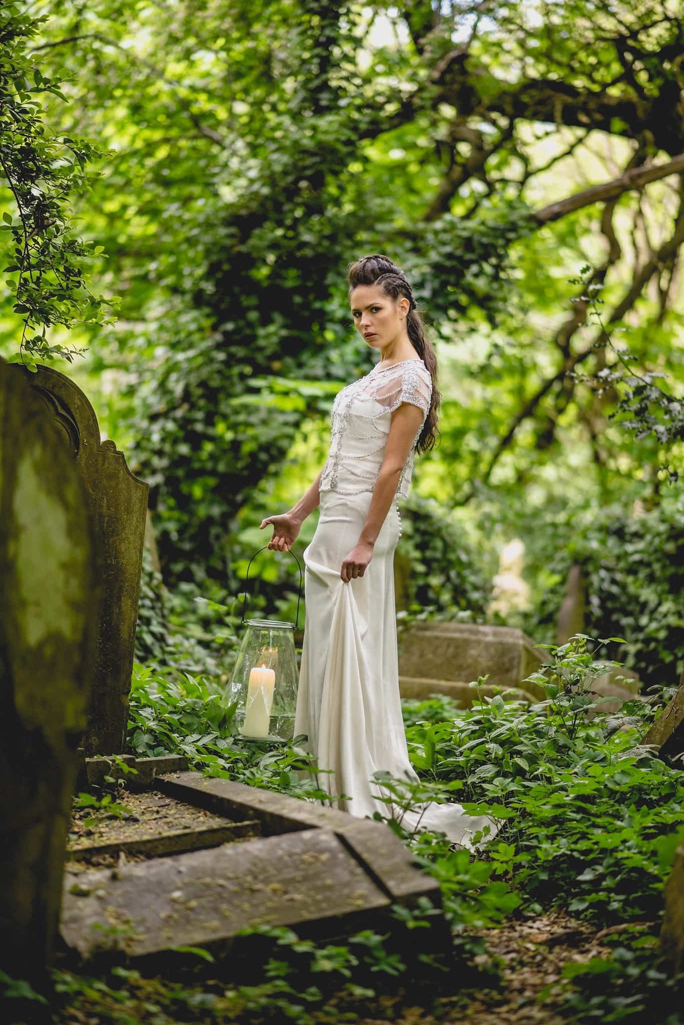 Bride stands among the graves in Abney Park, holding a lantern