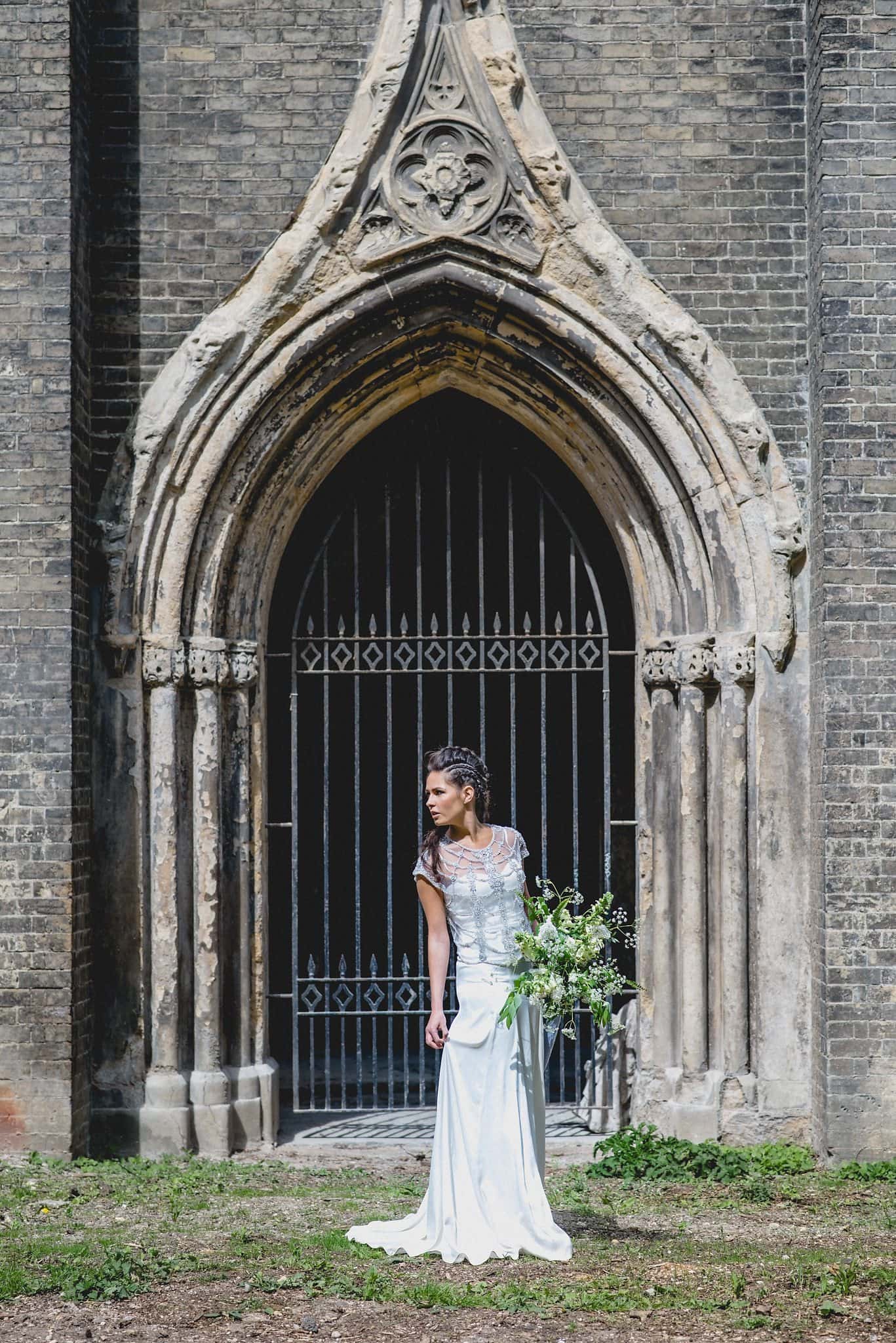 Bridal portrait in front of the entrance arch holding large bouquet of wild flowers