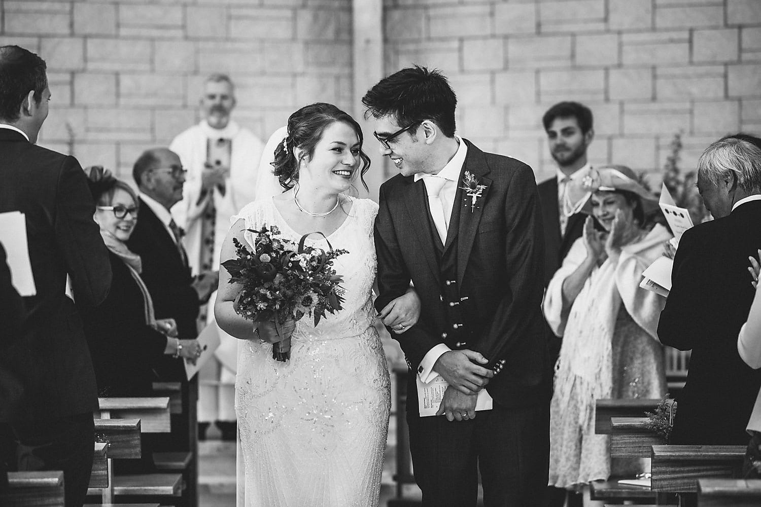 Bride and Groom walk down the aisle together smiling and gazing at each other