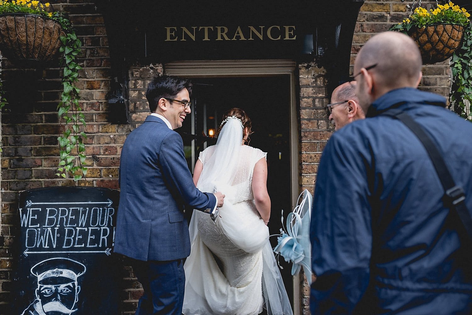 Groom holds up his bride's dress as she enters the pub