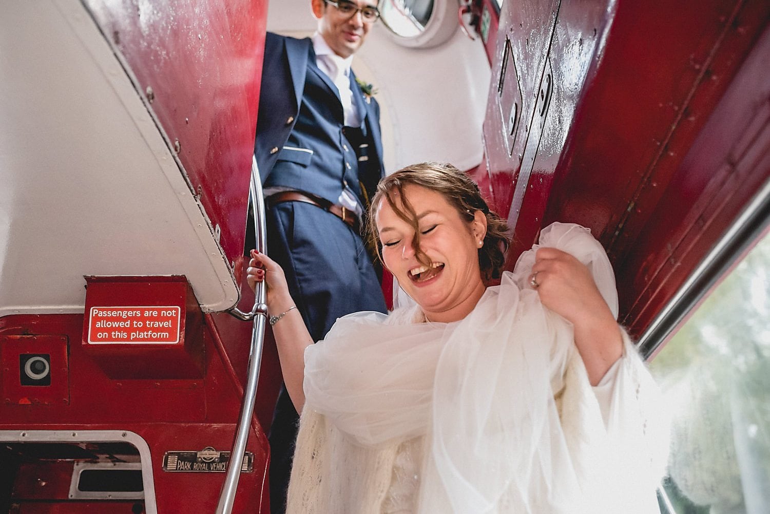 The bride laughs and holds up her dress as she makes it down the narrow stairs of the bus