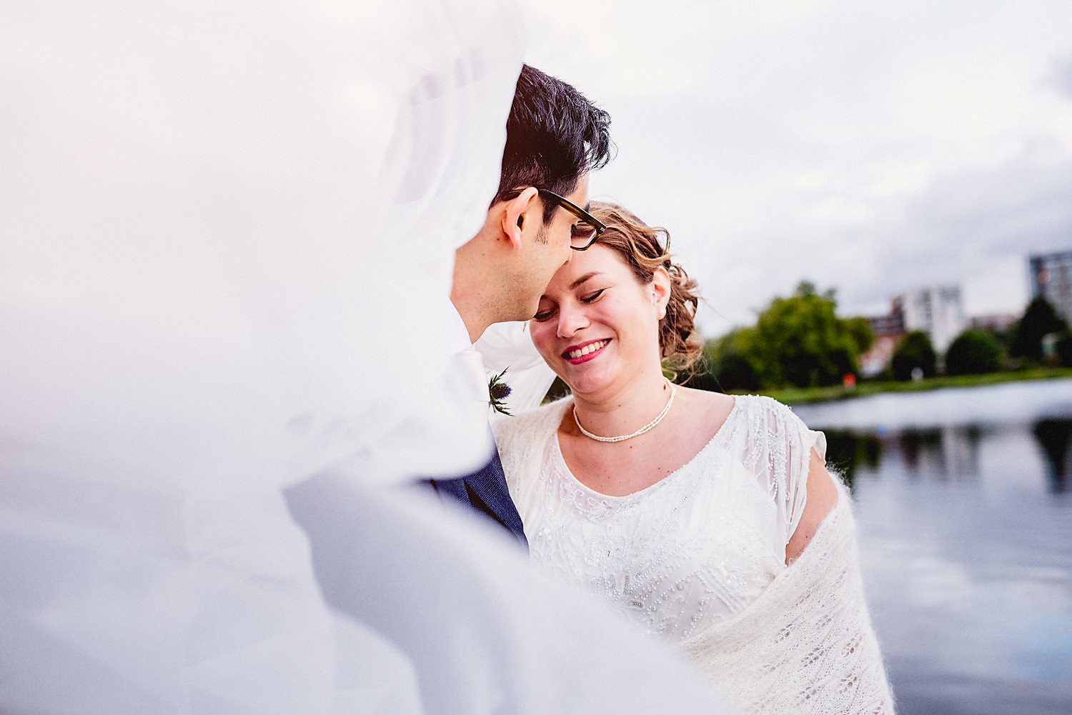 A portrait of the couple by the water, with the billowing veil in the foreground