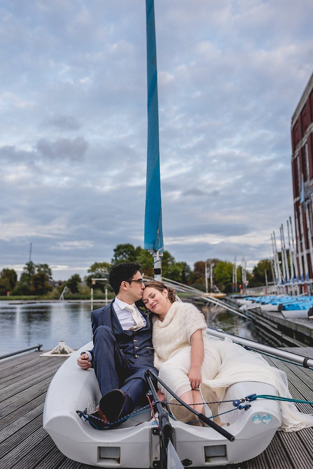 Bride and Groom sit in a sail boat on the jetty at the London West Reservoir Centre