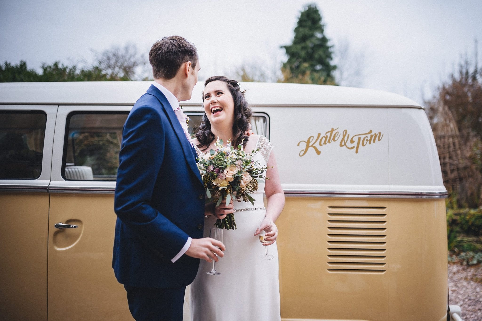 Bride and groom laugh together next to their personalised VW camper van