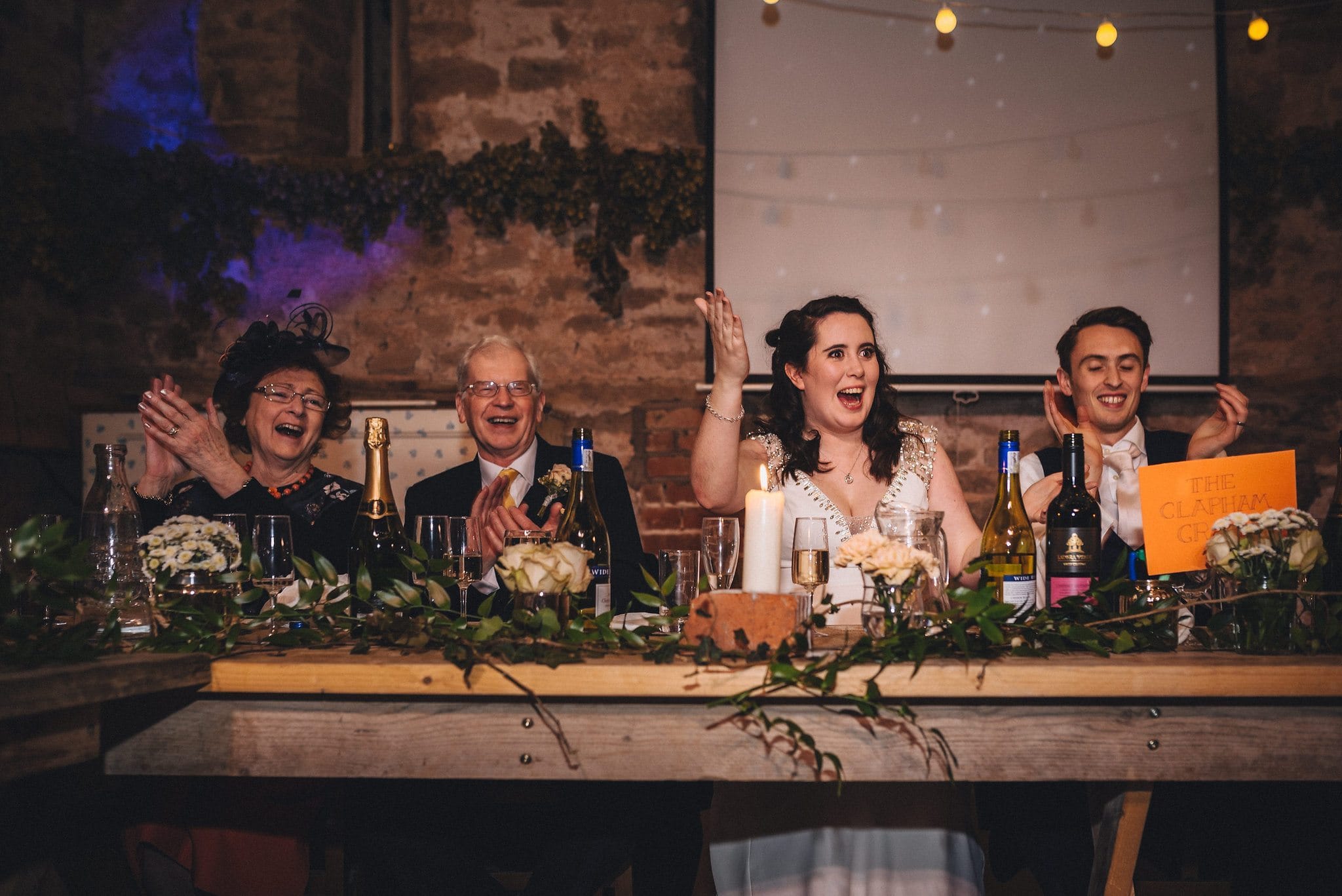 Bride gestures happily to her bridesmaids as they make a speech