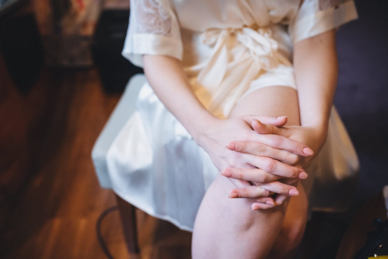 Bride sits on bed with hands clasped wearing silk dressing gown